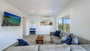 A modern living room with a sofa, a coffee table, and a painting of a beach scene.