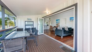 A covered outdoor area with a dining table and chairs, a sofa, and a kitchen in the background. - The Cottage - 16 Clarke Street (Bargara)