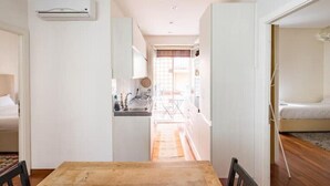 Una stanza compatta con un tavolo e sedie in legno, angolo cottura con lavello e fornelli, e un letto con materasso bianco.