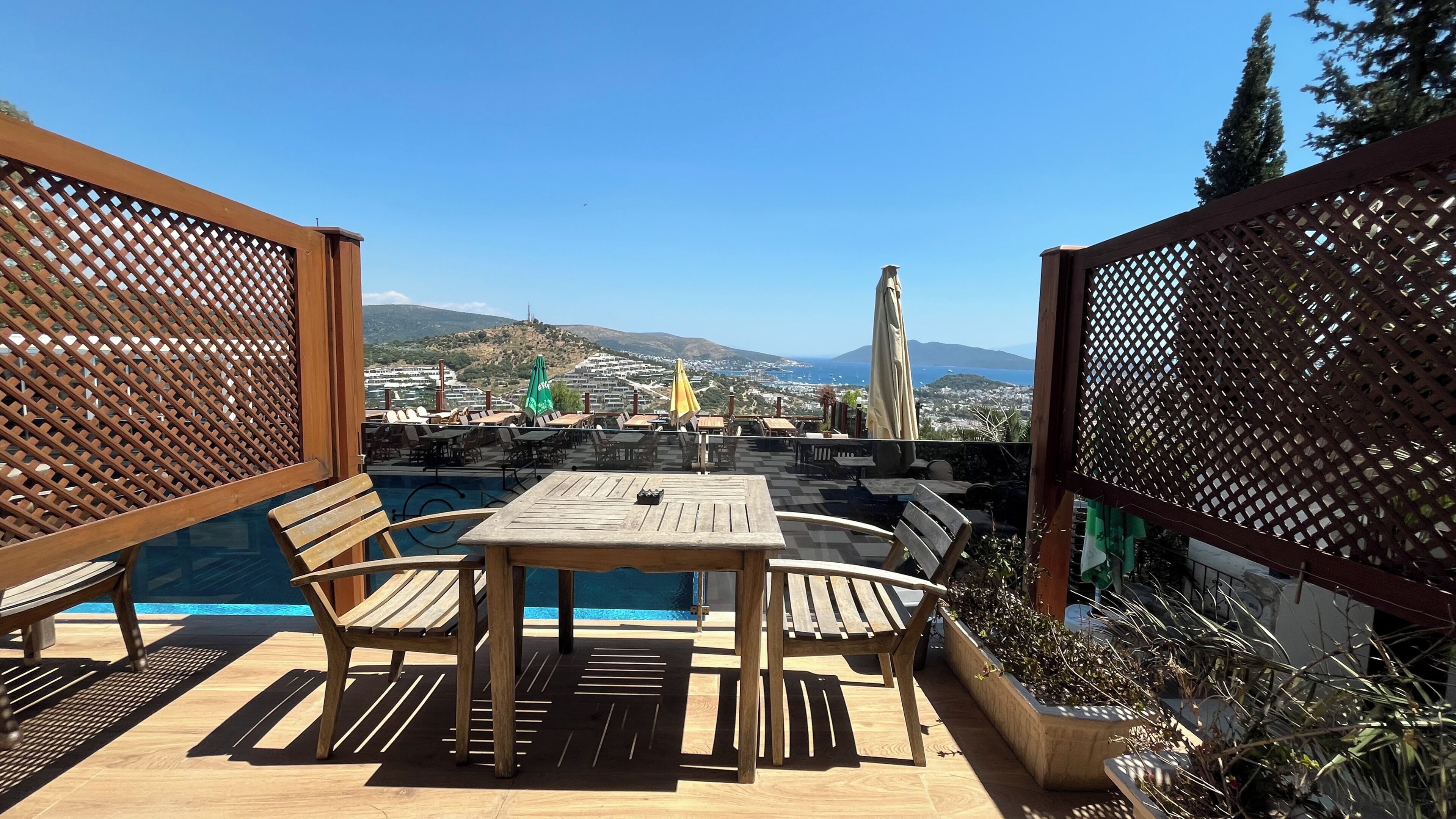 An outdoor pool area with wooden furniture and a view of a coastal town.