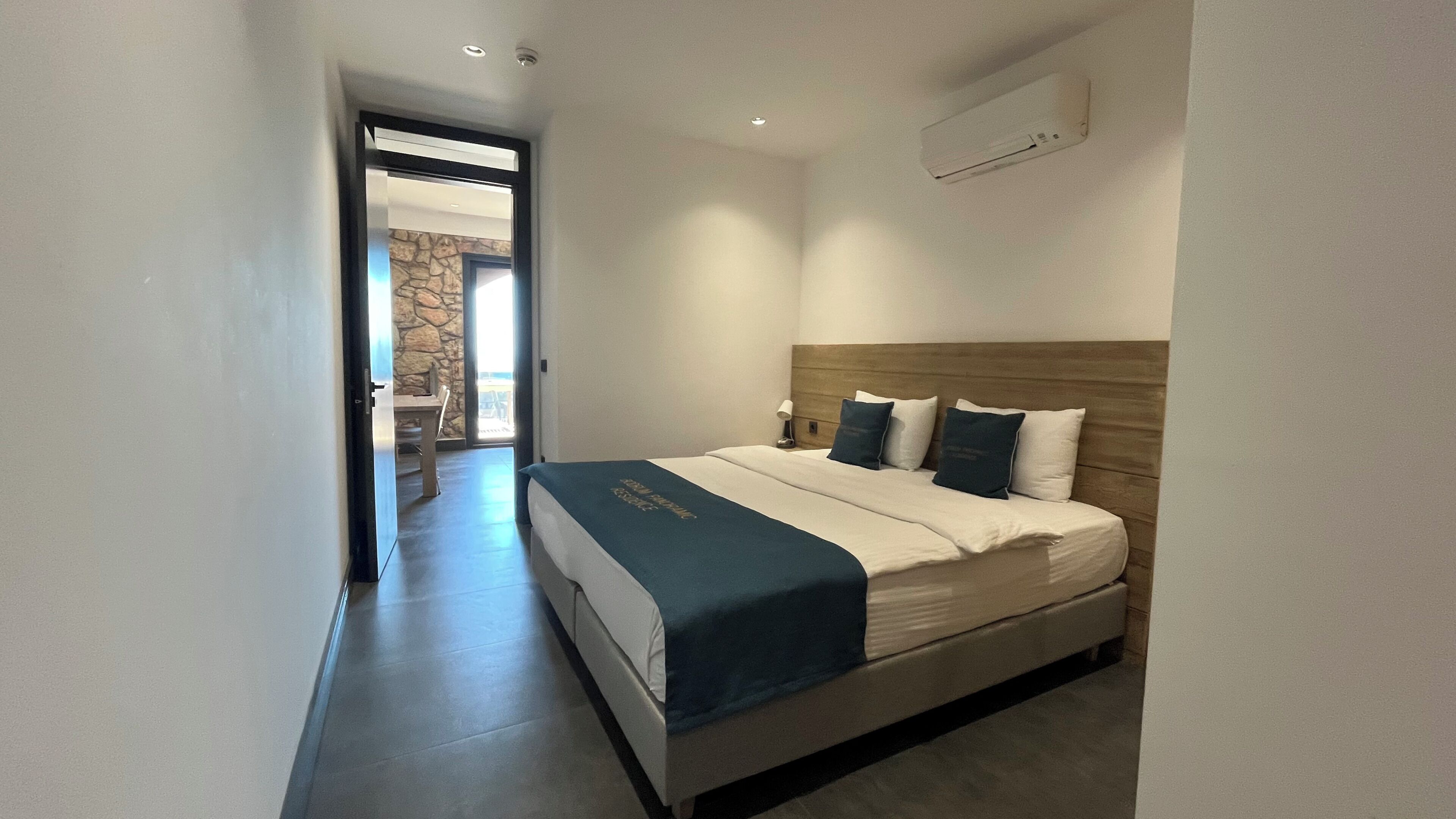 Habitación de hotel con una cama, una mesita de noche, una lámpara y vistas a un balcón.