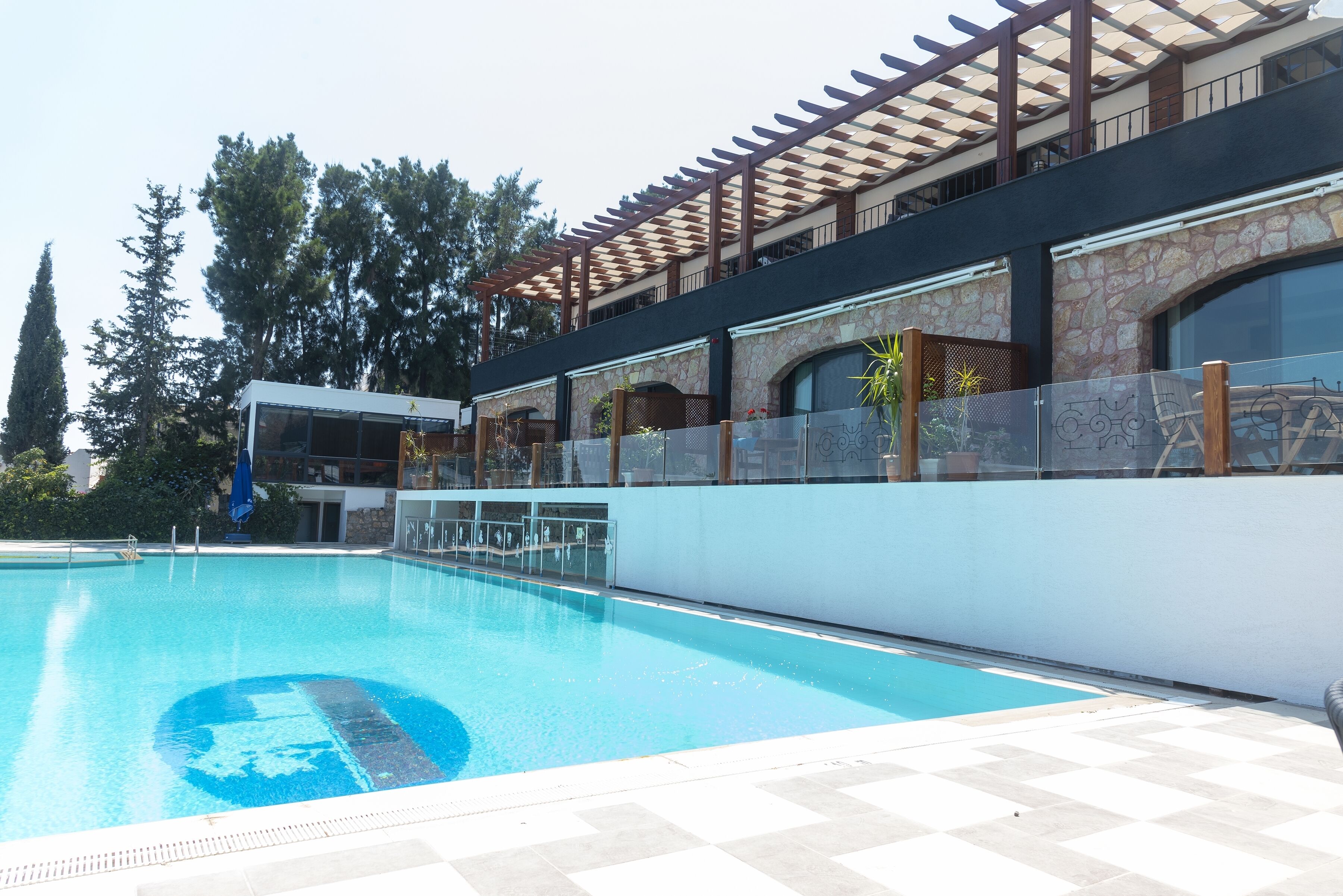 Una piscina con un pergolato e un muro in pietra.