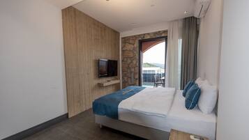 Una habitación de hotel moderna con cama, televisor, pared decorativa de piedra y balcón con vistas.