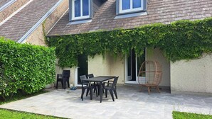 Ein Haus mit überdachter Terrasse, einem Esstisch, Stühlen und einem Korbstuhl.