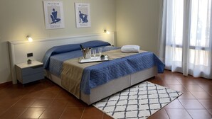 A neatly made bed with a blue quilt, a bedside table with a lamp, and two framed artworks on the wall. - 2 Bedroom Apartment in Realmonte (Realmonte)