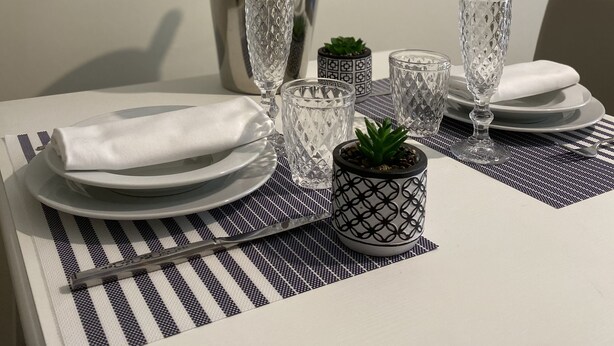 A dining table set with clear glassware, a metal pitcher, and a small potted plant. Two framed quotes about coffee are displayed on the wall. - 2 Bedroom Apartment in Realmonte (Realmonte)