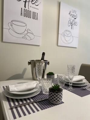 A dining table set with clear glassware, a metal pitcher, and a small potted plant. Two framed quotes about coffee are displayed on the wall. - 2 Bedroom Apartment in Realmonte (Realmonte)