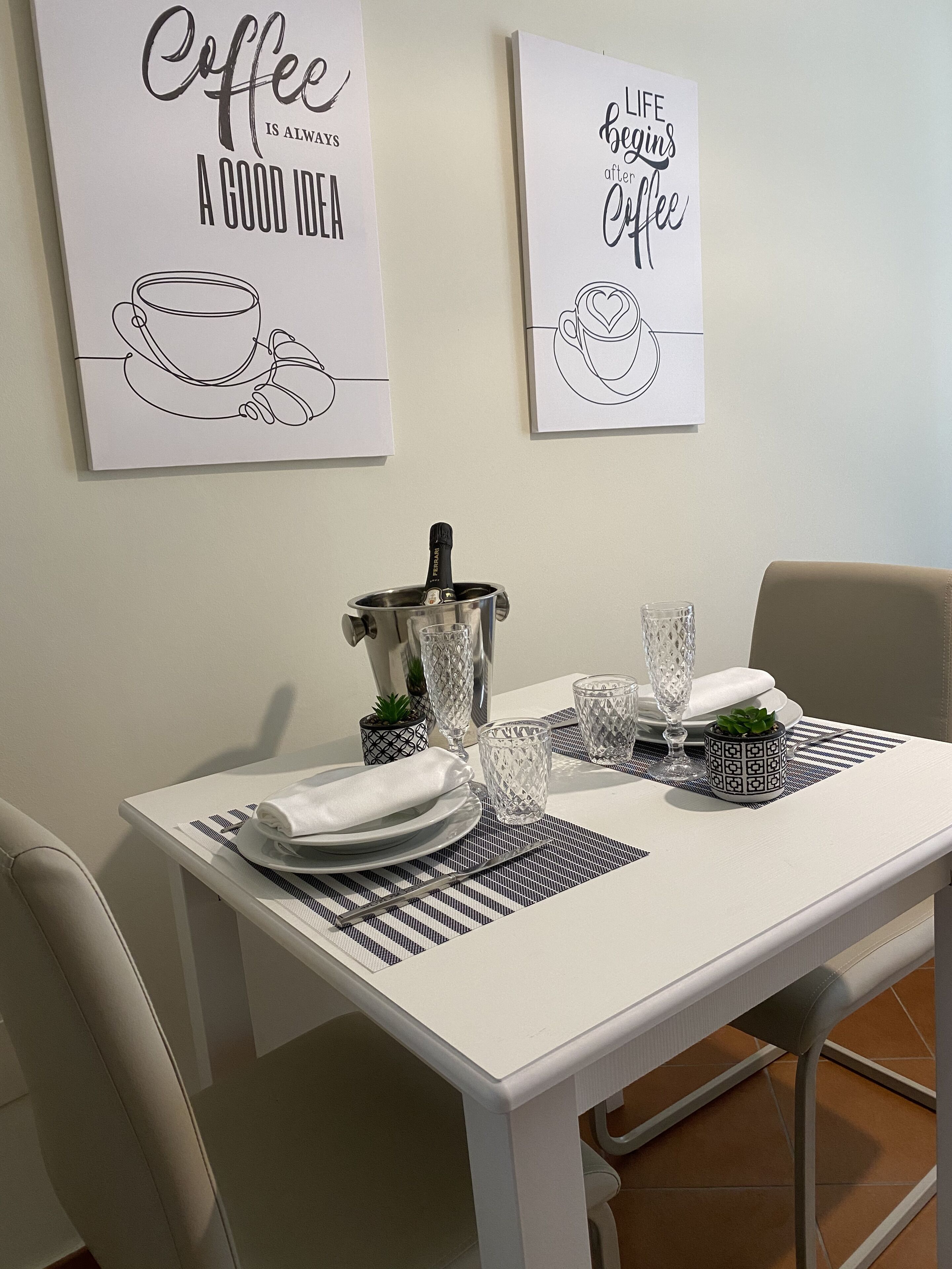 A dining table set with plates, glasses, and a coffee pot, with two wall art pieces above.