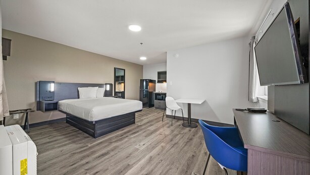 A hotel room with a bed, bedside tables, a desk, a chair, a TV, and a wardrobe.