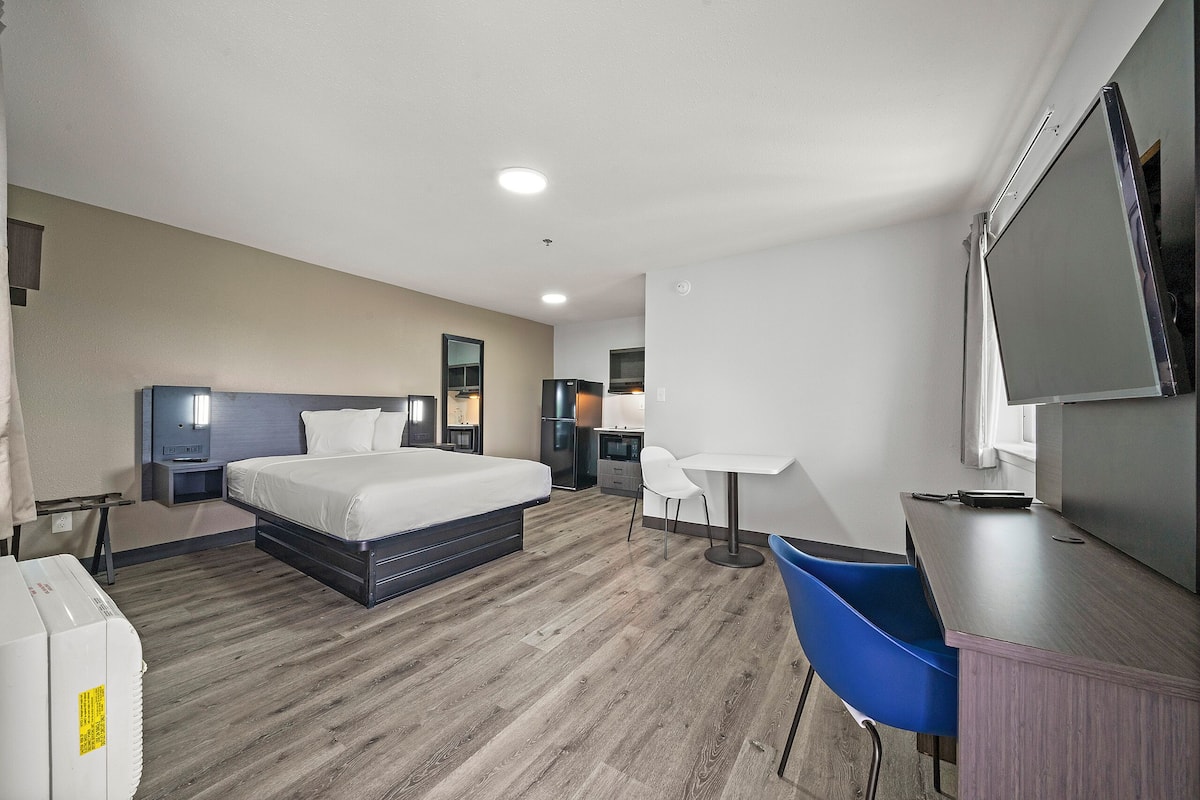Una habitación de hotel con cama, mesitas de noche, escritorio, silla, televisor y armario.