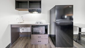 A compact kitchen with a built-in microwave, a stainless steel refrigerator, and a wooden cabinet under the countertop.
