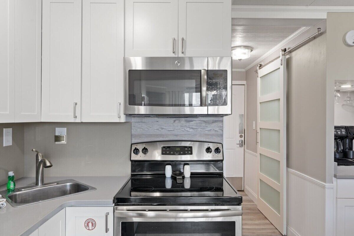 A kitchen with white cabinets, stainless steel appliances, a sink, and a door with frosted glass panels.