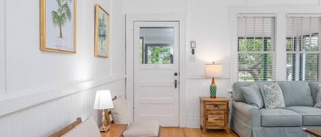Una sala de estar con un sofá gris, una mesita de noche de madera con una lámpara, una pequeña mesa de madera y un tapete floral.