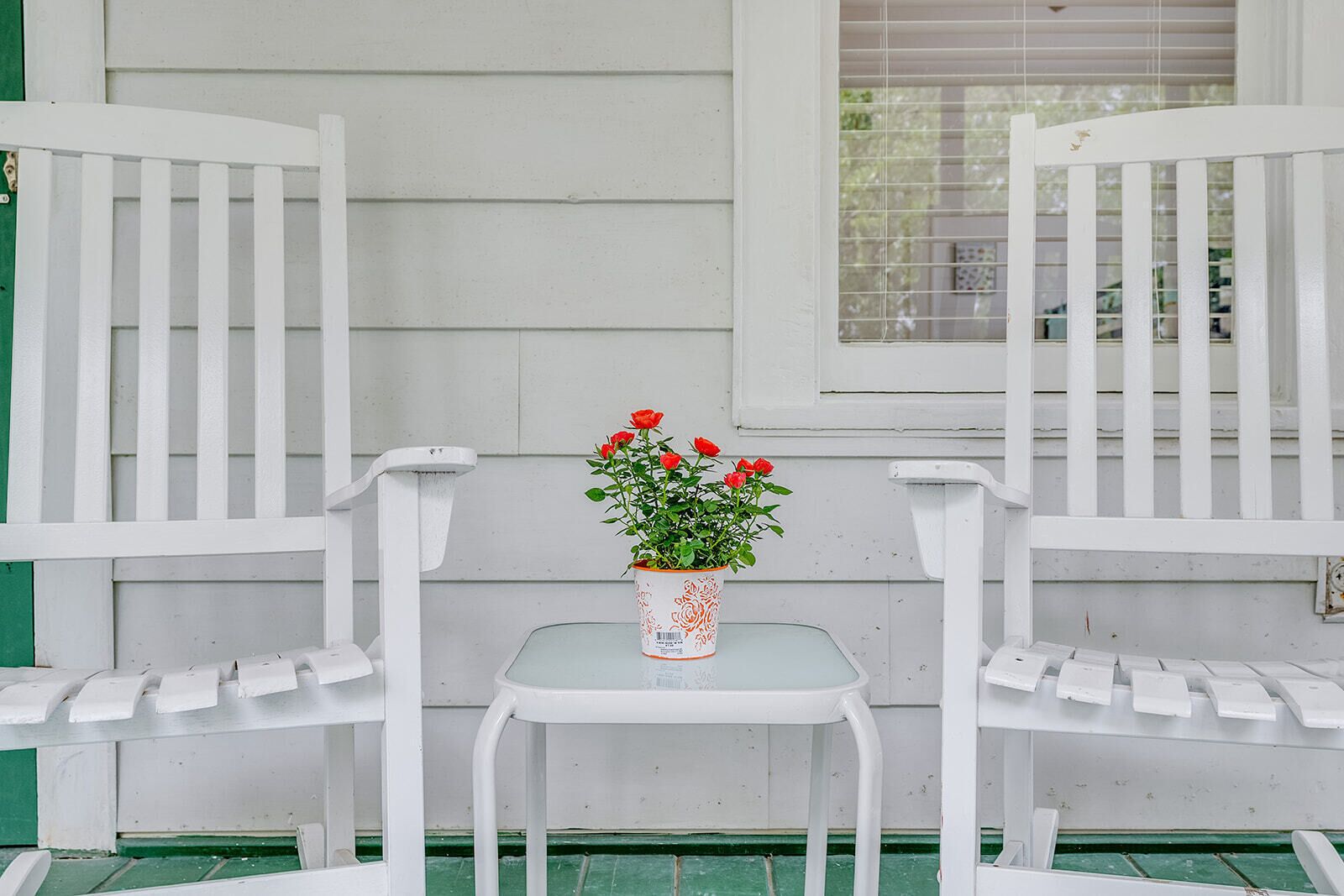 Två vita stolar med ett litet bord emellan, och en krukväxt med röda blommor placerad mellan dem.