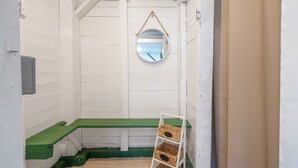 A small, narrow room with white walls and a green bench. A round mirror hangs on the wall, and a white ladder with baskets is against the wall. - Quaint and Cozy Beachside Cottage w/ Screened-In Porch by Tybee Cottages (Tybee Island)