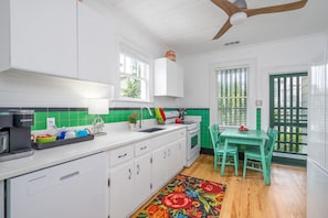 Una cocina con armarios blancos, salpicadero verde, suelo de madera y un área de comedor con mesa y sillas verdes.