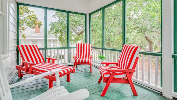 A covered porch with red and white striped chairs and a small table. - Quaint and Cozy Beachside Cottage w/ Screened-In Porch by Tybee Cottages (Tybee Island)