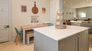 A modern kitchen with a central island, a dining area with chairs, and a living space with a sofa and a TV. - The Garden Flat (Bridport)