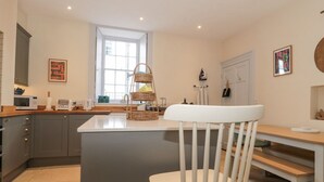 A modern kitchen with a central island, a white chair, and a window providing natural light. - The Garden Flat (Bridport)