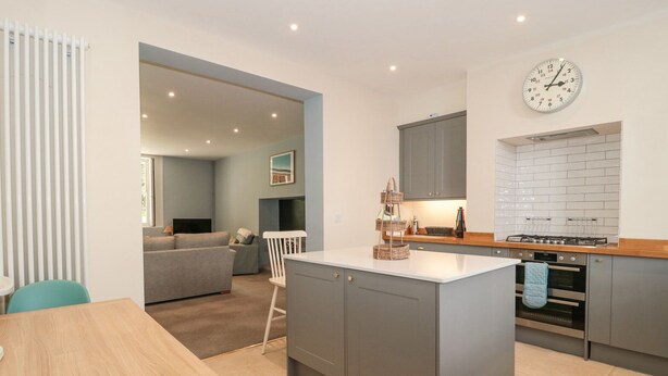 A modern kitchen with grey cabinets, a wooden dining table, and a built-in island. - The Garden Flat (Bridport)