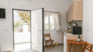 A compact kitchen with a sliding door leading to a balcony, a small dining table with chairs, and a microwave on the counter. - Experience Dreamy Santorini Gorgeous Std (Santorini)