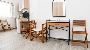 A compact kitchen with wooden cabinets, a dining table with chairs, and a small refrigerator. - Experience Dreamy Santorini Gorgeous Std (Santorini)