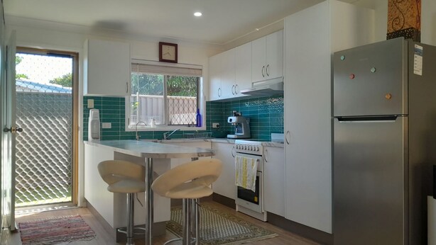 A compact kitchen with a refrigerator, a coffee maker, and a window with a view. - 2BR villa in quiet cul-de-sac with BBQ, herb garden, games, parking, (Evans Head)