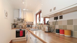 A compact kitchen with a dishwasher, oven, microwave, and kettle. - Teal House (Lyme Regis)