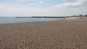 A pebbled beach with a calm sea, a pier extending into the water, and buildings in the background. - Teal House (Lyme Regis)