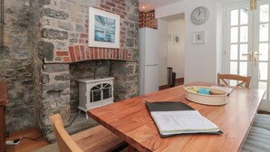 A cozy kitchen with a stone wall, a white refrigerator, a wooden dining table with chairs, and a clock on the wall. - Teal House (Lyme Regis)