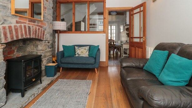 A cozy living room with a stone fireplace, a sofa, a leather couch, and a dining area visible through an open door. - Teal House (Lyme Regis)