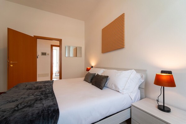 A hotel room with a bed, bedside table, lamp, and a patterned wall decoration. - Bright and Comfortable in Menaggio by Wonderful Italy (Menaggio)