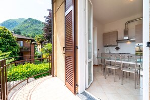 A modern kitchen with a glass dining table and chairs, a balcony with a metal railing, and a view of a lush green landscape. - Bright and Comfortable in Menaggio by Wonderful Italy (Menaggio)