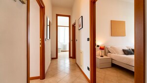 A hallway with wooden doors, a tiled floor, a bed with a nightstand, a lamp, and a framed picture on the wall. - Bright and Cozy in Menaggio by Wonderful Italy (Menaggio)