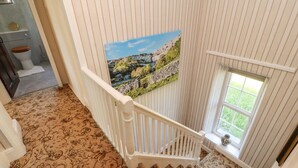 A staircase with a patterned carpet, a white railing, and a window with a view of greenery. - Rose Cottage (Settle)