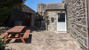 A stone building with a wooden door, a stone wall, and a picnic table. - Rose Cottage (Settle)