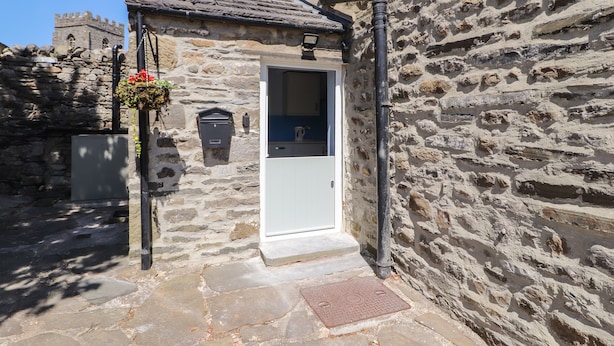 A stone building with a white door, a mailbox, and a small window. - Rose Cottage (Settle)