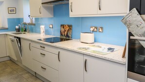 A kitchen with white cabinets, a blue backsplash, a toaster, and a dishwasher. - Rose Cottage (Settle)