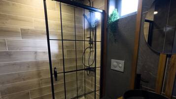 A modern bathroom with a wooden floor, a glass-enclosed shower, a round sink, and a mirror.