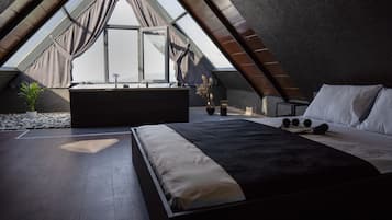 A bedroom with a large bed, a small table, and a window with curtains.