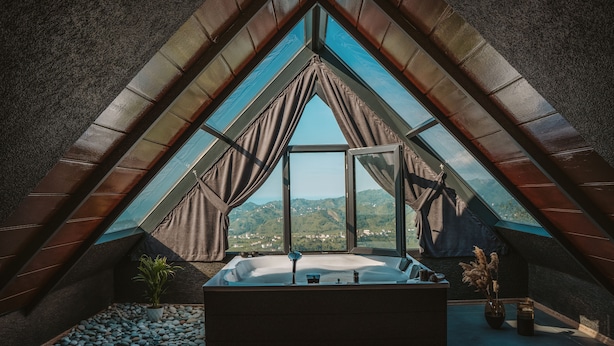 A modern bathroom with a large skylight, a bathtub, and a view of the mountains.