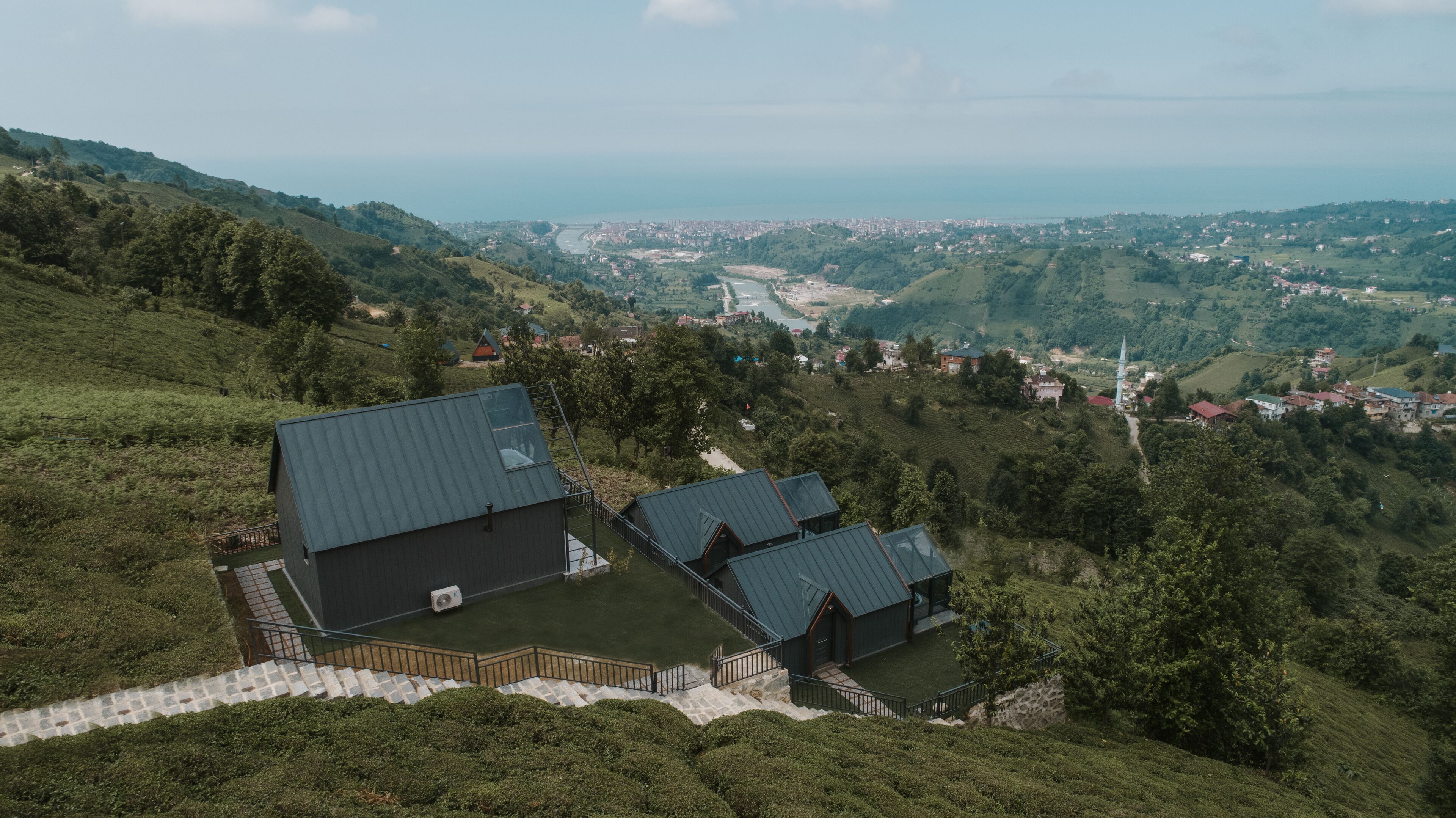 A hillside property with a modern building featuring a large flat roof and a smaller attached structure.