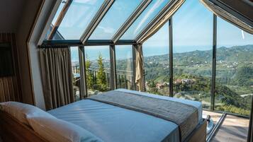 A bedroom with a large skylight, a bed, and a view of a hilly landscape.