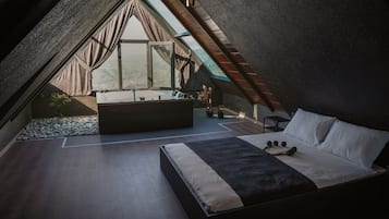 A modern bedroom with a large bed, a small seating area, and a view of the outdoors.