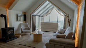 A cozy living room with a fireplace, a comfortable sofa, a coffee table, and a large window offering a view of the outdoors.