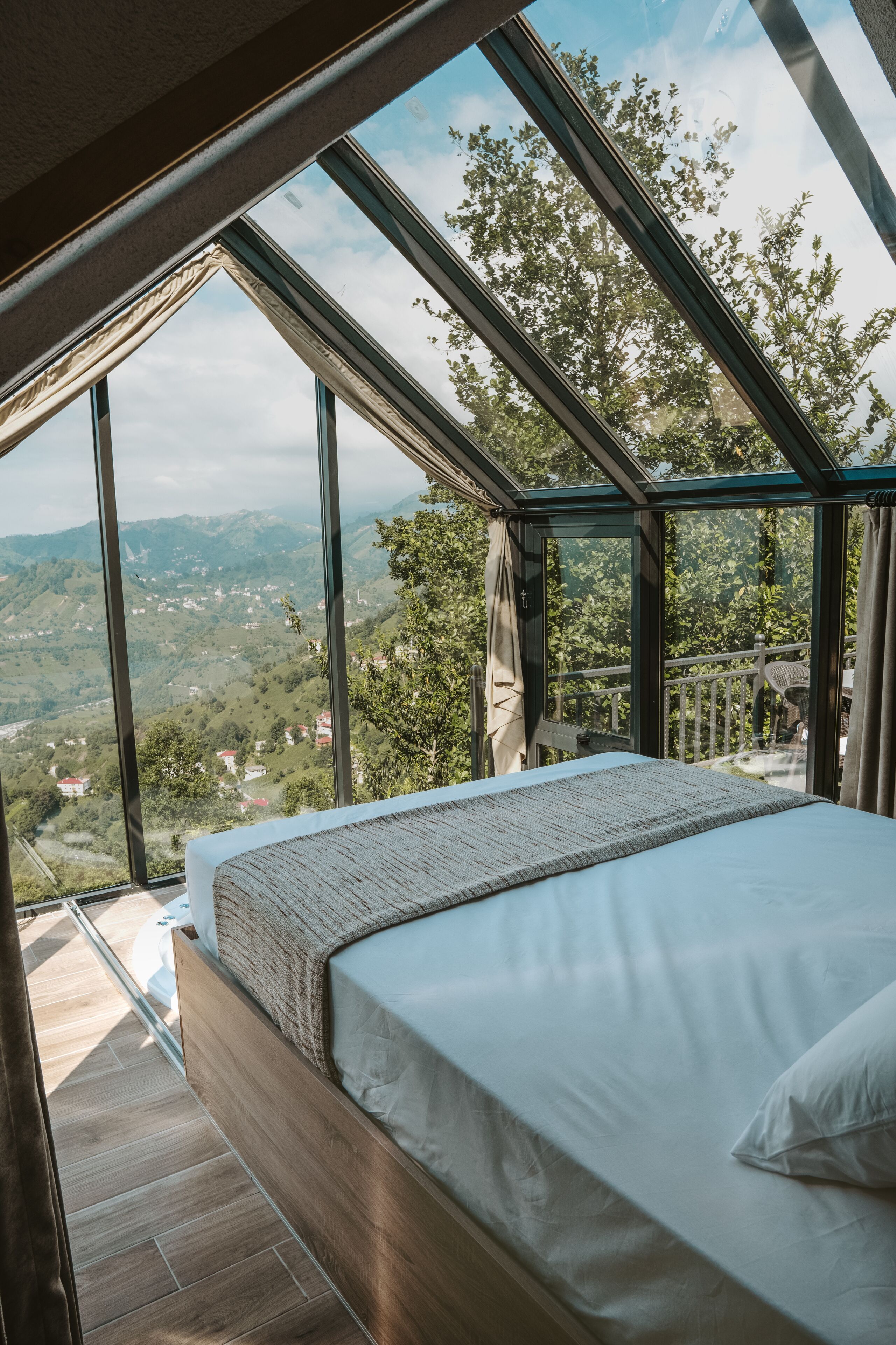 Un dormitorio con un tragaluz grande, una cama de madera y vistas a un paisaje montañoso.