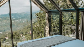 Un dormitorio con un tragaluz grande, una cama de madera y vistas a un paisaje montañoso.
