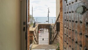 Une vue à travers une porte donnant sur une zone côtière, avec une porte en bois rustique, un portail en métal et une statue de mouette posée sur un poteau.