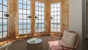 Une pièce dotée de trois grandes fenêtres donnant sur une étendue d’eau, d’une petite table ronde et d’une chaise en bois avec un coussin.