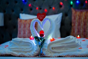 A neatly folded bed with a rose centerpiece and a heart-shaped towel arrangement.